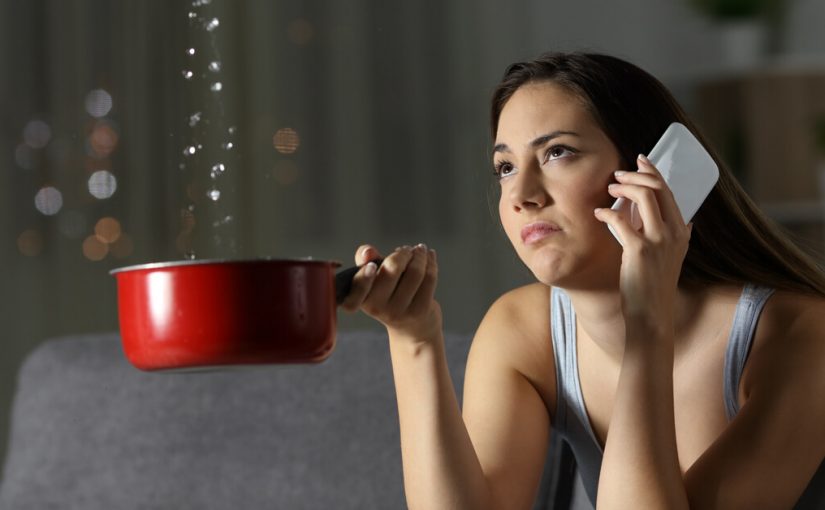 woman on phone with roof repair holding pot catching water